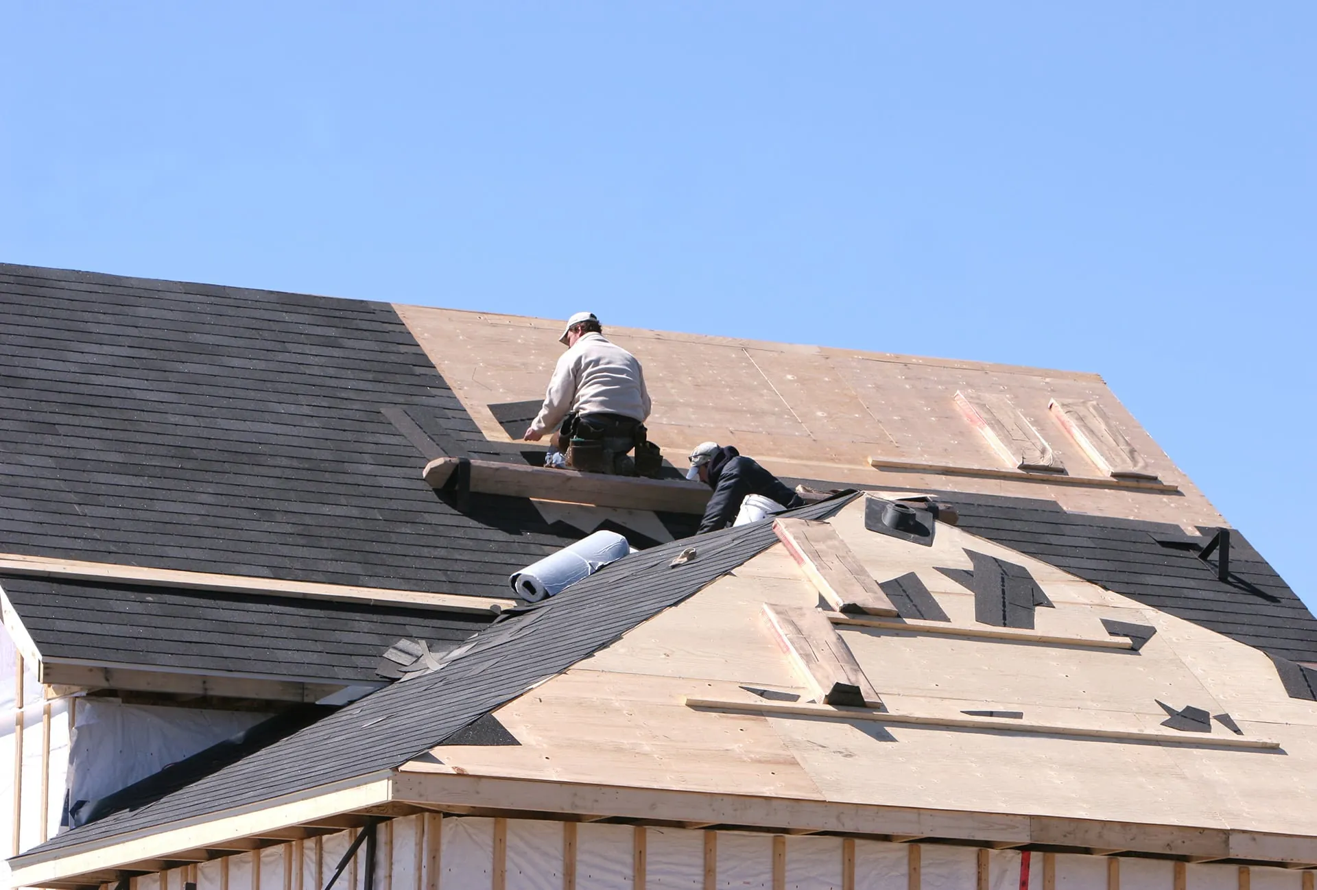Roofers installing shingles beside exposed roof decking. Roofers installing shingles beside exposed roof decking.