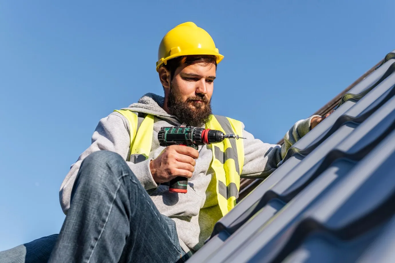 Worker in a yellow hard hat using a drill on a roof.